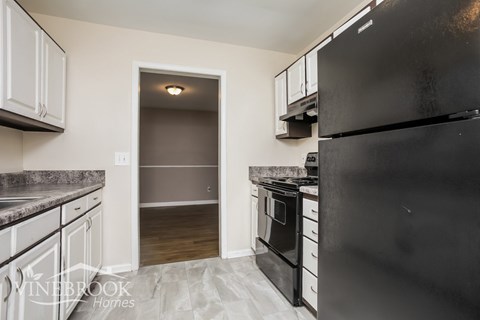 A kitchen with a black refrigerator and white cabinets.