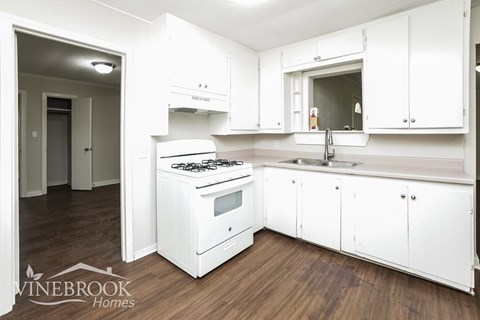 A white kitchen with a stove, sink and cabinets.
