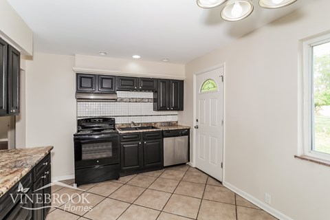 A kitchen with black appliances and a tiled floor.