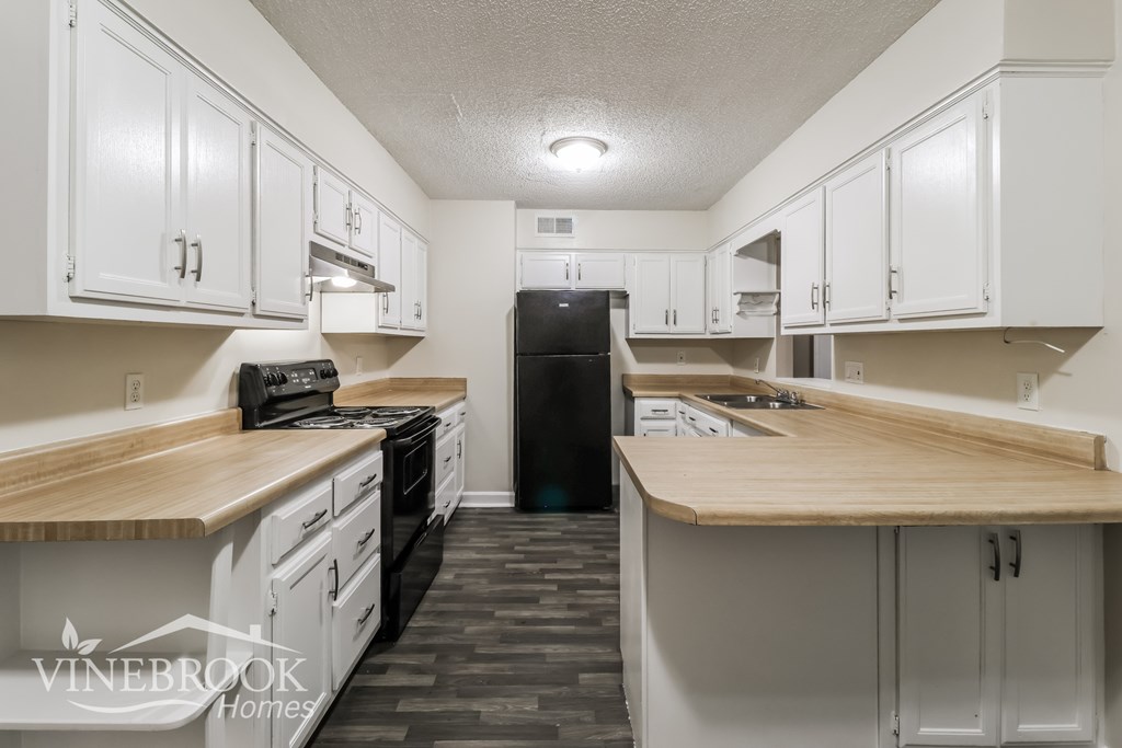 A kitchen with white cabinets and a black refrigerator.