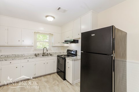 A black refrigerator sits in a kitchen with white cabinets and a marble countertop.