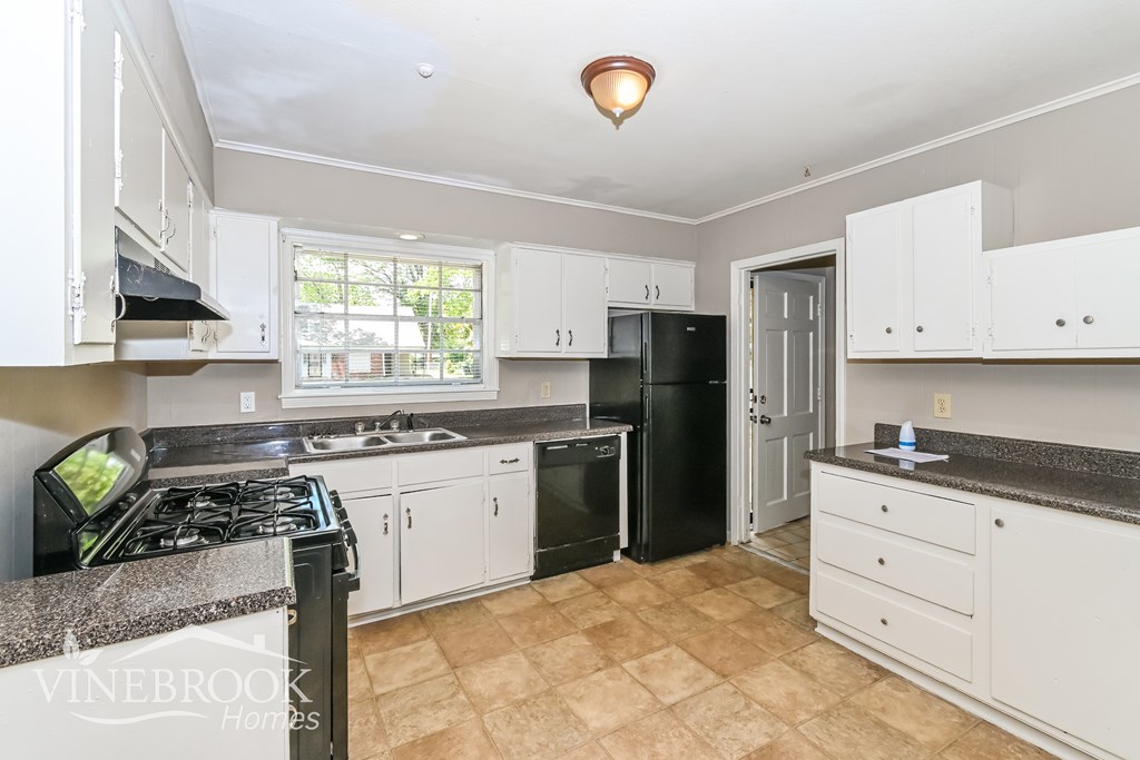 A kitchen with a black refrigerator and white cabinets.