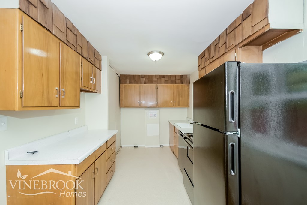 A kitchen with wooden cabinets and a black refrigerator.