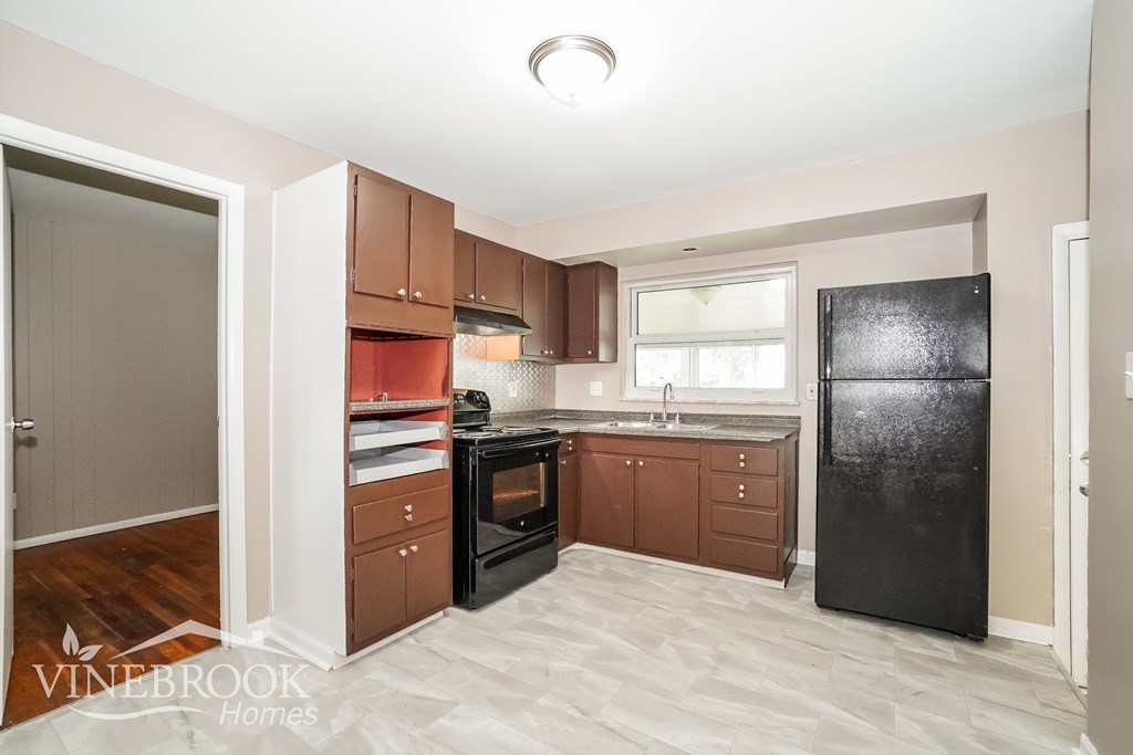 A kitchen with a black fridge, brown cabinets, and a window.