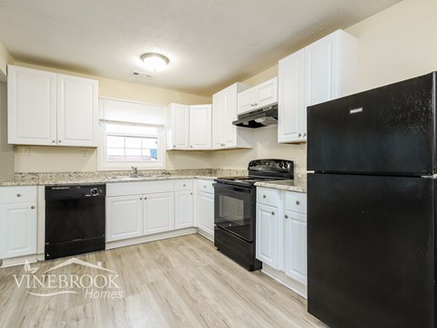 A black refrigerator is in a kitchen with white cabinets.