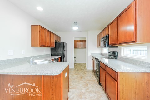 A kitchen with wooden cabinets and a Vinebrook Homes logo.