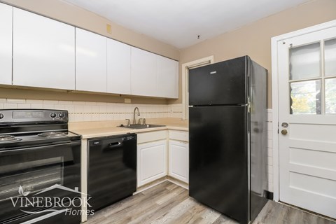 A black refrigerator stands in a kitchen with white cabinets.