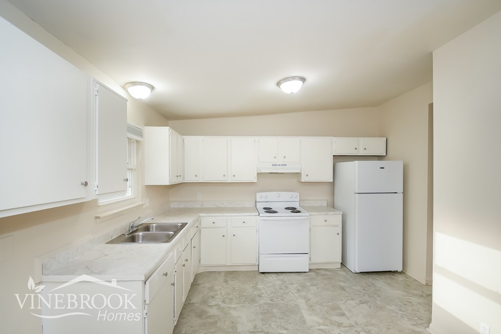 A white kitchen with a sink, stove, and refrigerator.