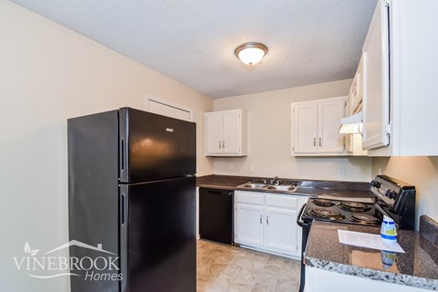 A kitchen with a black fridge and white cabinets.