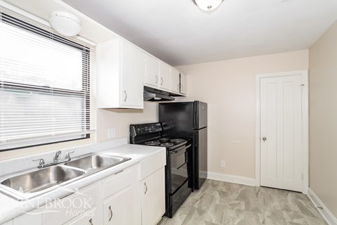 A kitchen with a black refrigerator and white cabinets.