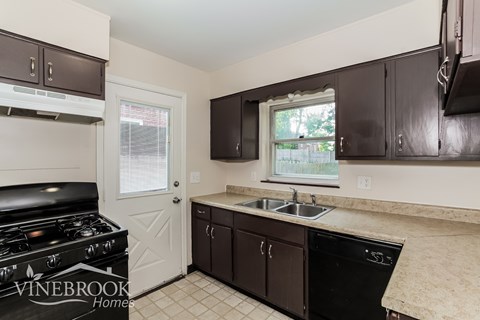 A kitchen with a black stove top oven and dark brown cabinets.