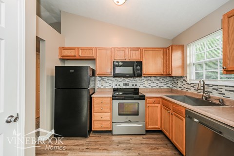 A kitchen with wooden cabinets and a black fridge.
