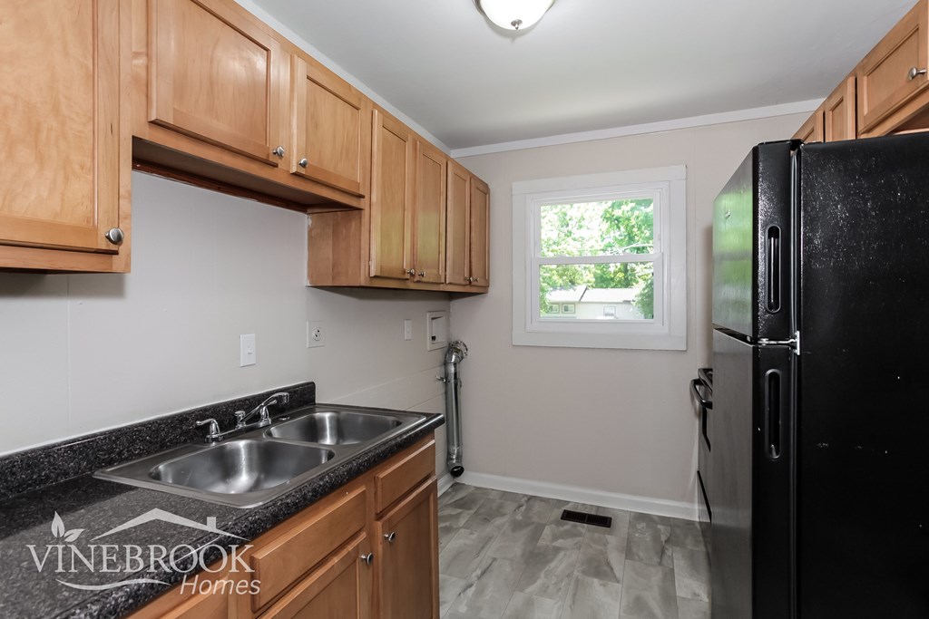 A kitchen with wooden cabinets and a black refrigerator.