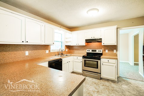 A kitchen with white cabinets and a Vinebrook Homes logo.