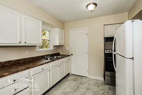 A kitchen with white cabinets and a white fridge.