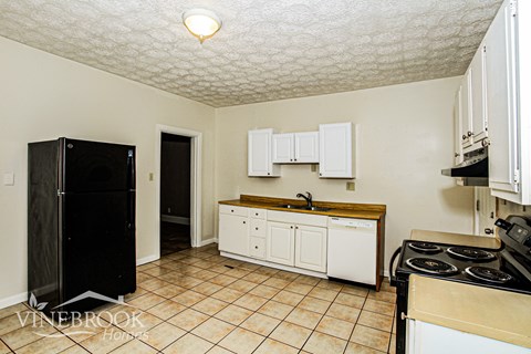 A kitchen with a black fridge, white cabinets, and a tiled floor.