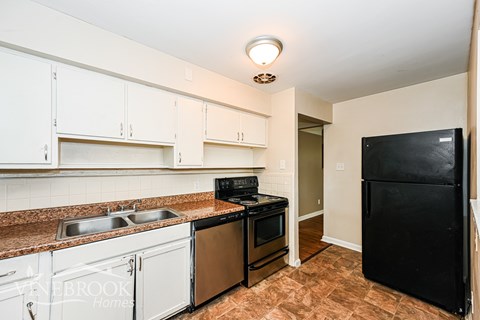 A kitchen with white cabinets and a black fridge.