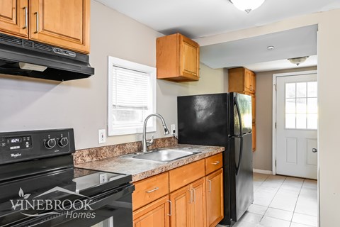 A kitchen with a black refrigerator, wooden cabinets, and a stove top oven.