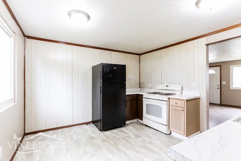 A black refrigerator sits in a kitchen with white cabinets and a white stove.