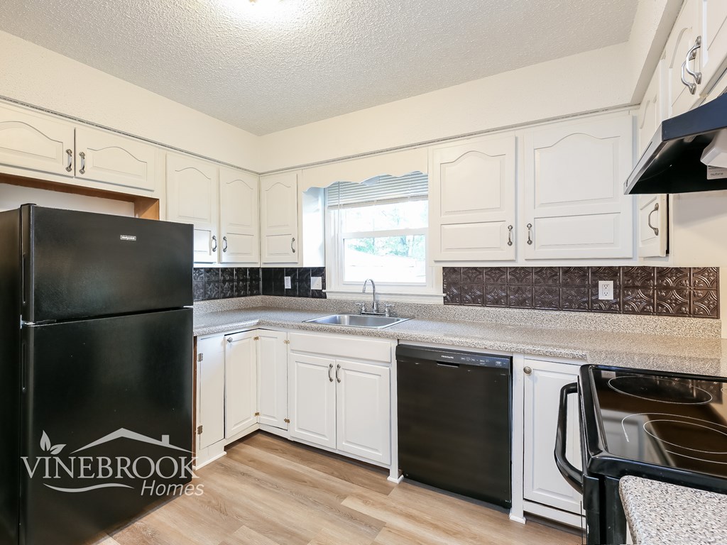 A kitchen with white cabinets and a black fridge.