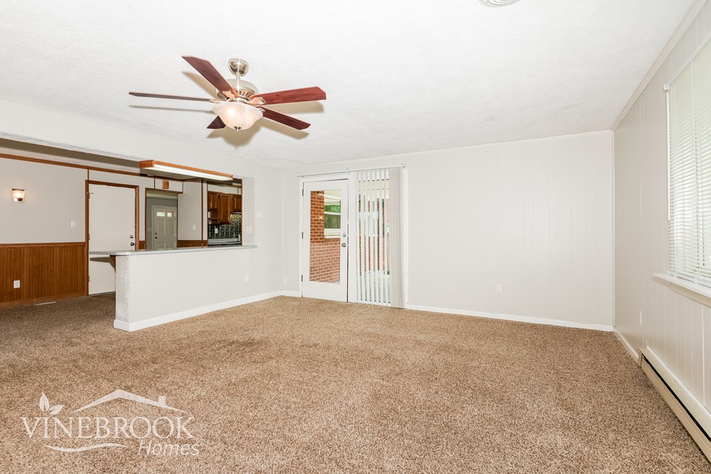 an empty living room with a ceiling fan and a kitchen
