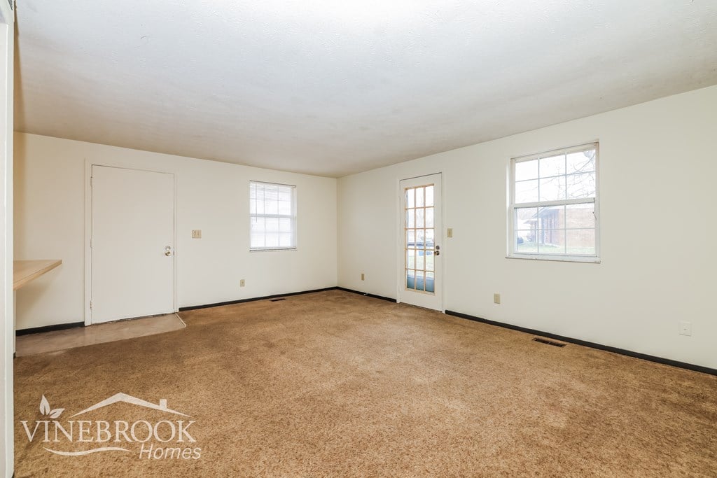 A room with a carpeted floor and two windows.