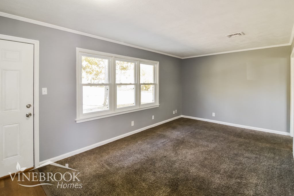 A room with a carpeted floor and a window with a view of trees outside.