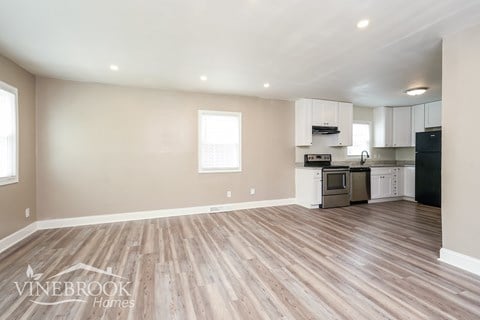 A spacious room with wood flooring and a kitchen area in the background.