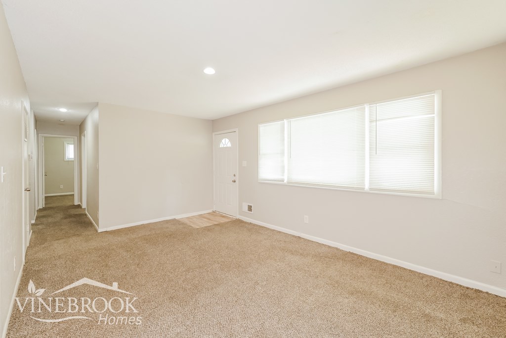 A spacious room with carpeted floor and two windows.