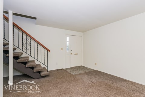 A carpeted room with a staircase leading to the upper floor.