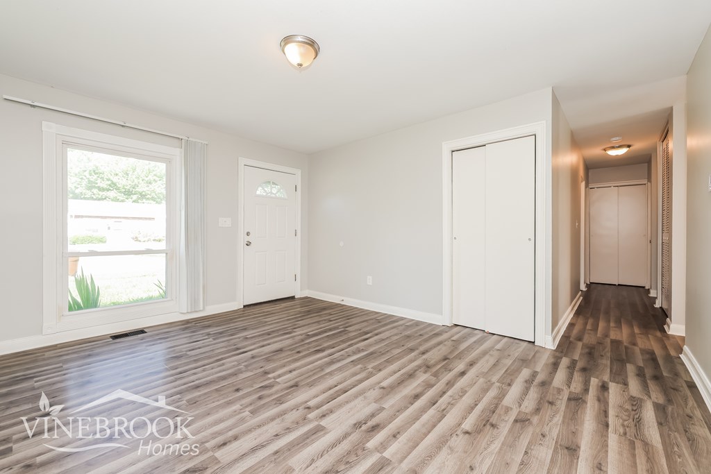 A room with wooden flooring and white walls, with a window and a door visible.