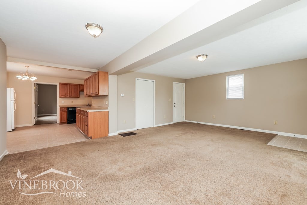 A spacious room with beige carpeting and a logo that reads "Vinebrook Homes".