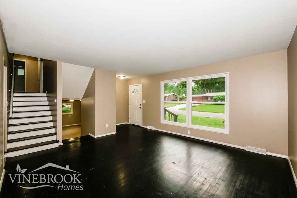 A room with a staircase and a window overlooking a green lawn.