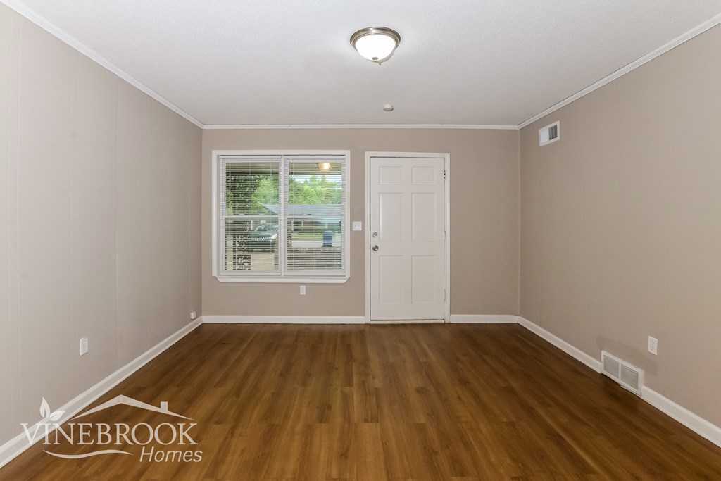 A room with a white door and a window with a view of trees and a building outside.