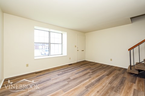 A room with wooden flooring and a staircase on the right side.