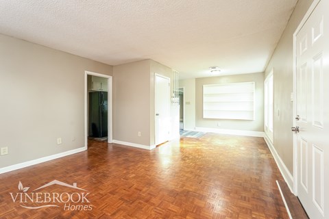A room with wooden floors and white walls, with a door on the right and a window on the far wall.