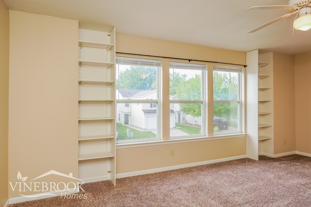 A room with a carpeted floor, a ceiling fan, and a window with blinds.