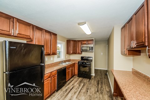 A kitchen with wooden cabinets and a black fridge.