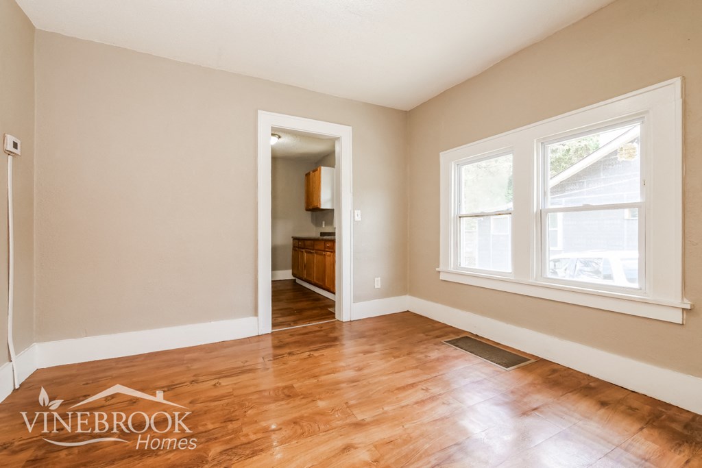 the living room and dining room of a home with wood flooring and white walls