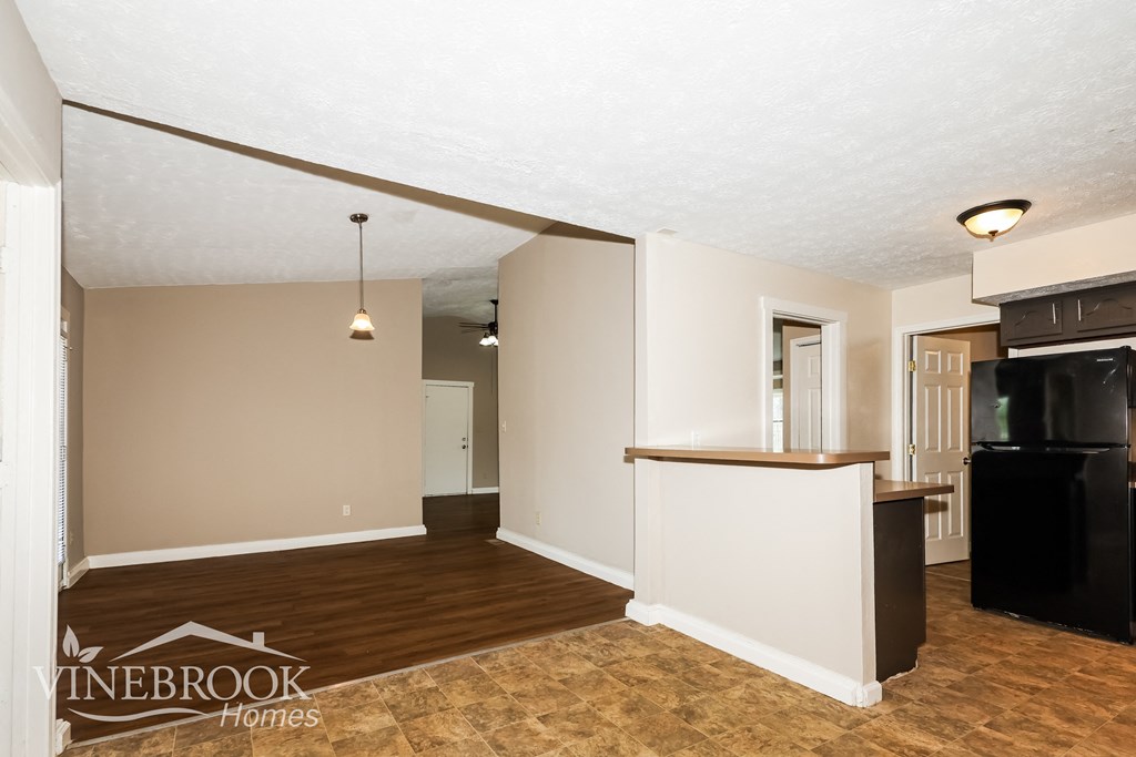 an empty living room with a kitchen and a black refrigerator
