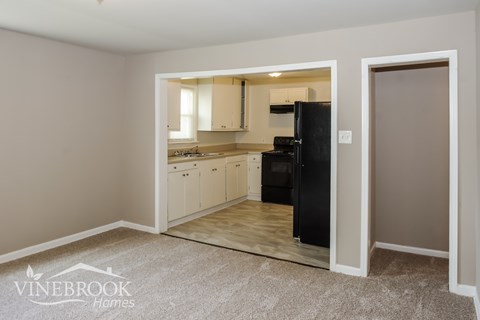 A kitchen area with a black fridge and cabinets is visible through an open door.