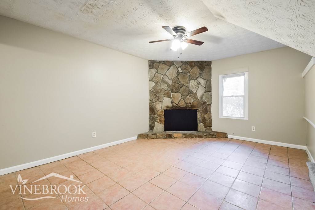 the living room has a stone fireplace and tile flooring