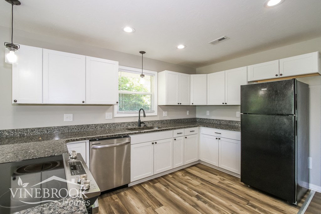 A kitchen with white cabinets and a black refrigerator.
