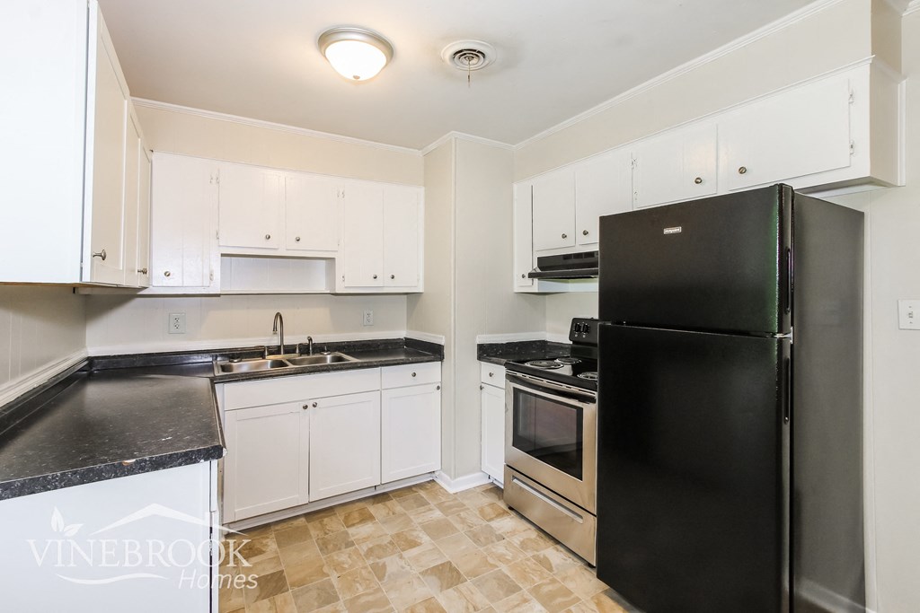 a kitchen with white cabinets and black counters and a refrigerator