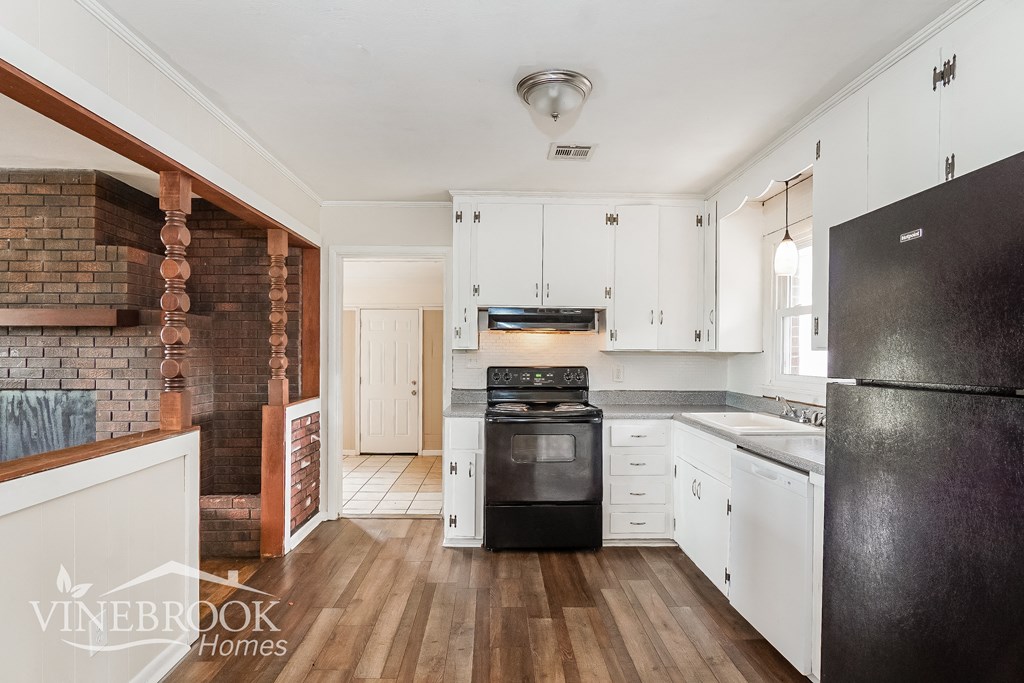 a kitchen with white cabinets and black appliances and a brick wall