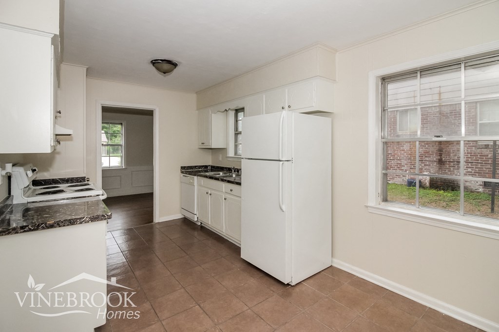 A kitchen with white appliances and a window overlooking a brick wall.