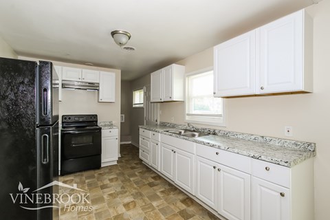 a kitchen with white cabinets and a black refrigerator and a sink