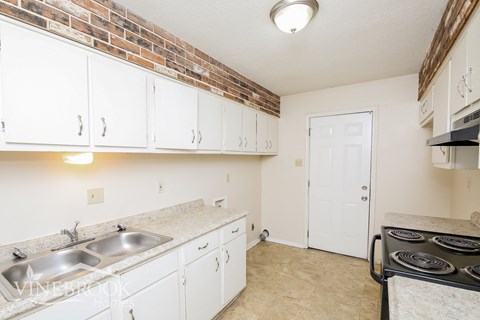 A kitchen with white cabinets and a brick wall.