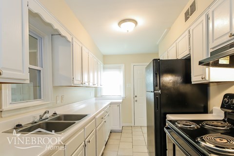 A kitchen with white cabinets and a black refrigerator.
