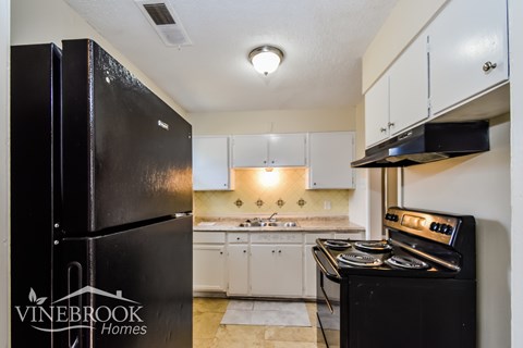 A black fridge in a kitchen with white cabinets and a black stove.